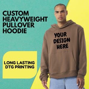 May include: A brown custom heavyweight pullover hoodie with a front pocket and a hood. The text "YOUR DESIGN HERE" is printed on the front. The background is a mix of teal and yellow.