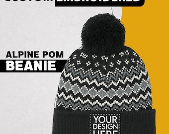 May include: Black and white Alpine pom beanie with a geometric pattern and a large black pom. The beanie has a black cuff with the text "YOUR DESIGN HERE" in a white box. The top of the beanie has a black pom.