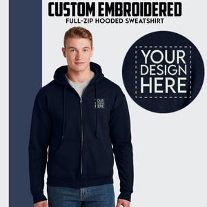 Peut inclure: Un sweat à capuche bleu marine à fermeture éclair intégrale avec un motif brodé blanc qui dit "YOUR DESIGN HERE" sur le devant.