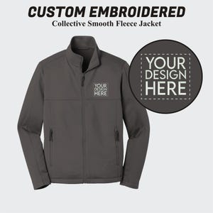 May include: A dark gray fleece jacket with a zipper closure and two pockets. The jacket has a space for a custom embroidered design on the left chest with the text "YOUR DESIGN HERE".
