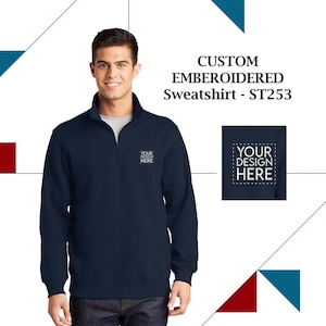 May include: A navy blue sweatshirt with a mock neck and zipper. The sweatshirt has the text "YOUR DESIGN HERE" embroidered on the left chest.