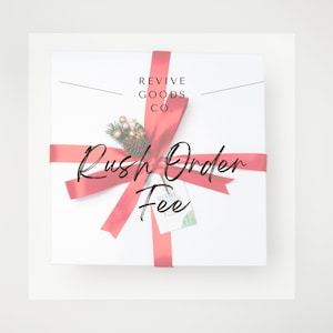 May include: A white gift box tied with a red ribbon, decorated with a sprig of greenery and a pinecone. The words "Revive Goods Co." are printed at the top, with "Rush Order Fee" in cursive script across the front. A small tag is attached.
