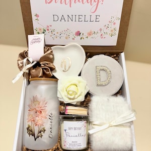 May include: A birthday gift box containing a candle, a decorative dish, a scrunchie, and a fluffy item. The box is decorated with floral designs and the words "Happy Birthday Danielle". The candle is labelled "Jasmine".