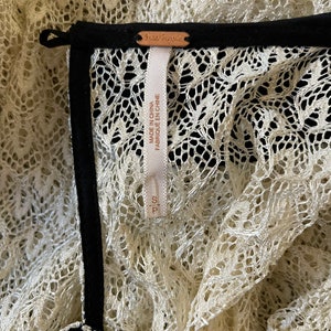 May include: Close-up of a white lace garment with a black trim and a Free People tag. The tag says "Made in China, Fabrique en Chine".