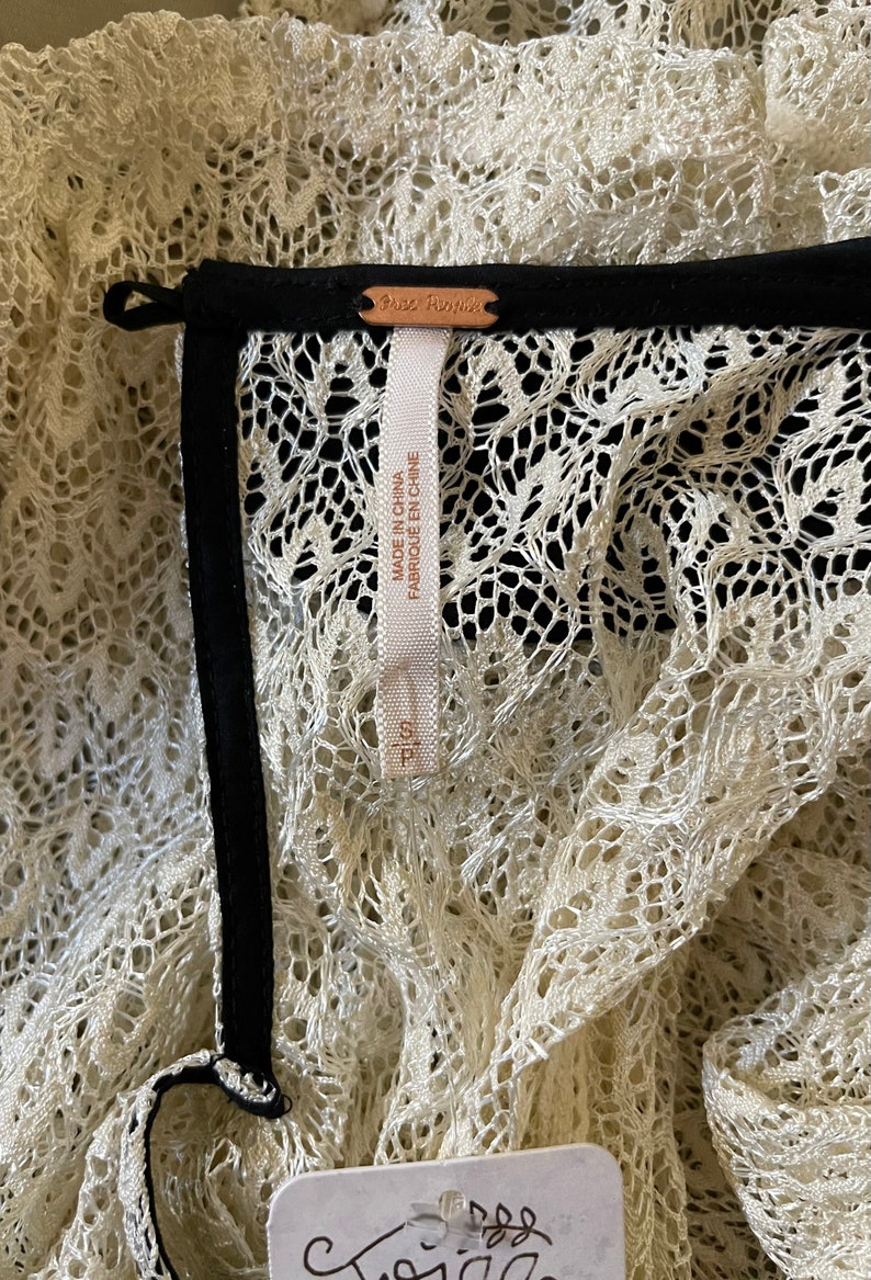 May include: Close-up of a white lace garment with a black trim and a Free People tag. The tag says "Made in China, Fabrique en Chine".