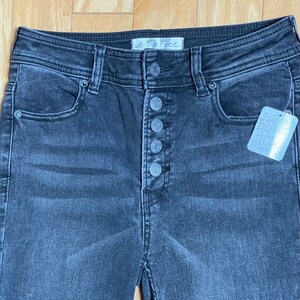 May include: Black high-waisted jeans with a button fly and a We The Free tag. The jeans have a distressed look and are made of a soft, comfortable denim.
