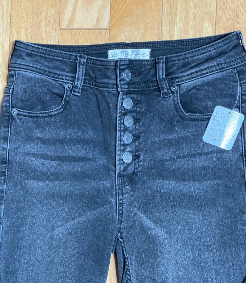 May include: Black high-waisted jeans with a button fly and a We The Free tag. The jeans have a distressed look and are made of a soft, comfortable denim.