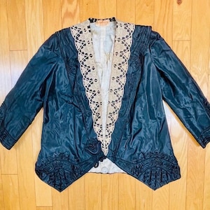 May include: A black satin jacket with a lace trim around the collar and cuffs. The jacket has a long, pointed tail and a decorative button closure.