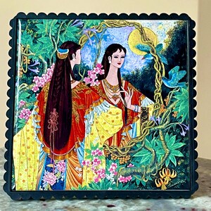 Puede incluir: Azulejo decorativo cuadrado con una ilustración de inspiración asiática de dos mujeres con trajes rojos y amarillos ornamentados, rodeadas de exuberante vegetación, flores y pájaros. El azulejo tiene un marco negro festoneado.