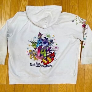 K&ouml;nnte beinhalten: Wei&szlig;er Kapuzenpullover mit einem bunten Aufdruck von Mickey Mouse und seinen Freunden, die 2014 in Walt Disney World feiern. Der Pullover hat Sterne auf den &Auml;rmeln.