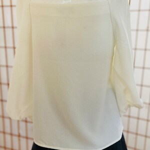 May include: A white, off-the-shoulder blouse with long, puffy sleeves. The blouse is made of a lightweight fabric and has a relaxed fit.