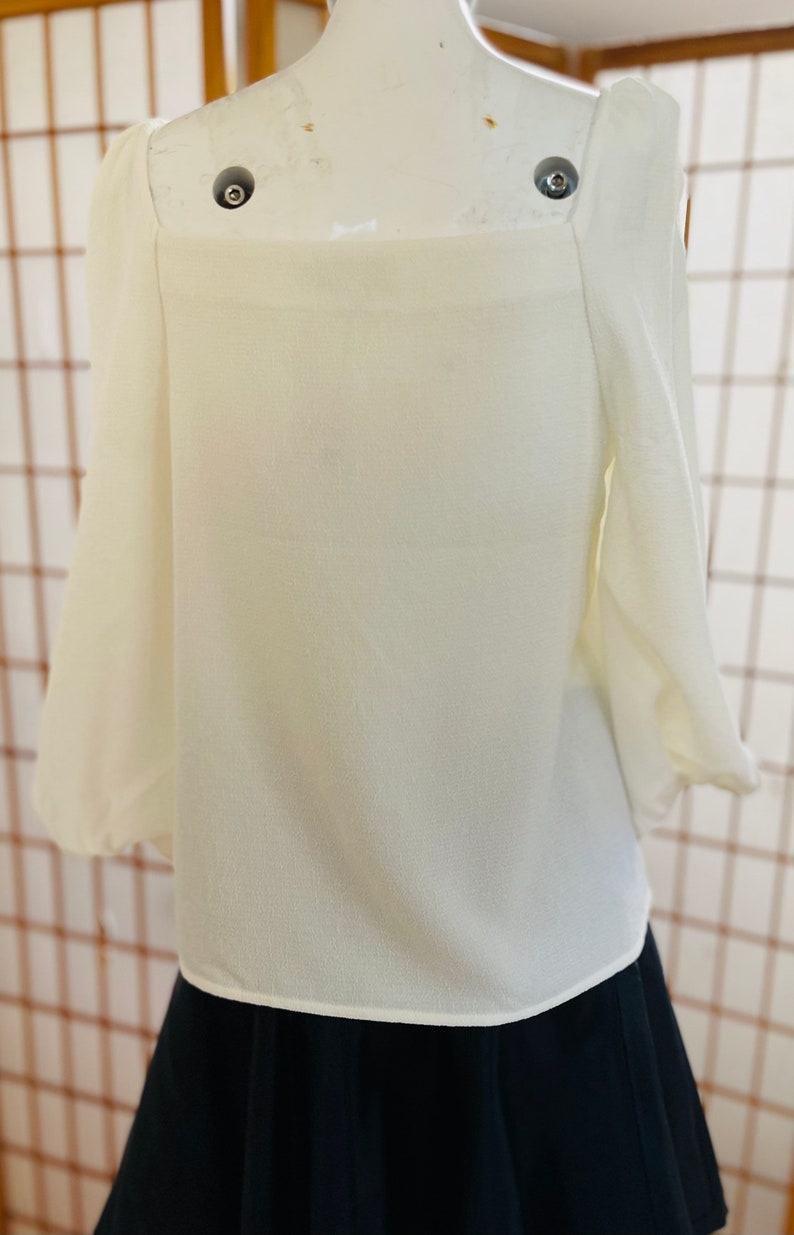 May include: A white, off-the-shoulder blouse with long, puffy sleeves. The blouse is made of a lightweight fabric and has a relaxed fit.