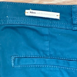 Puede incluir: Primer plano de pantalones de color verde azulado con un bolsillo trasero y una etiqueta que dice "Pilero and the Letterpress". Los pantalones tienen costuras visibles y un dise&ntilde;o cl&aacute;sico.