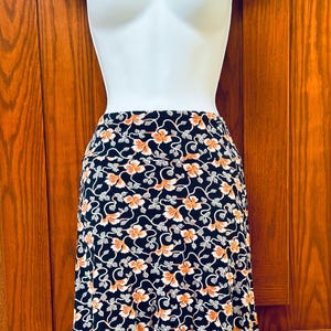 May include: A black skirt with a floral pattern in orange and white, displayed on a white mannequin. The skirt has a high waist and a flowing design, perfect for a casual or semi-formal look.