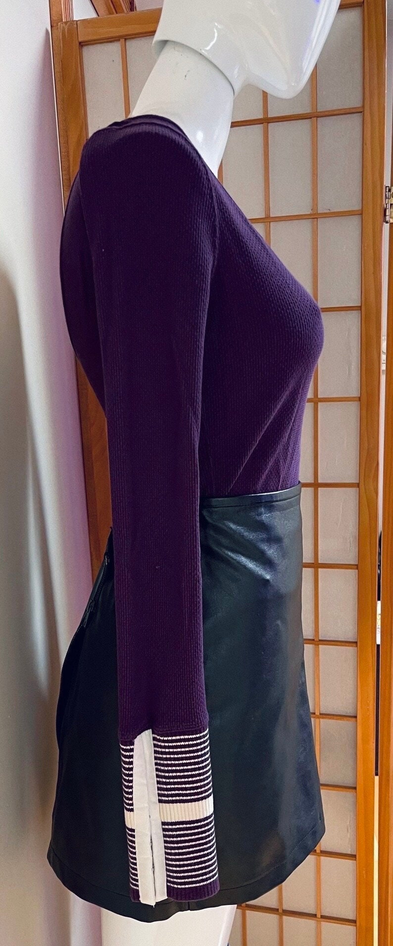 May include: A purple long-sleeved shirt with white striped cuffs and a black leather skirt.