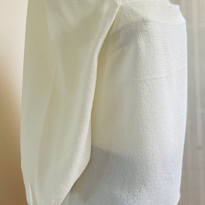 May include: A white, textured,  square-neck blouse with puffed sleeves. The blouse is cropped and has a fitted silhouette.