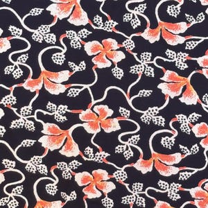 May include: A close-up of a fabric with a repeating floral pattern. The design features orange and white flowers with white vines and leaves against a dark navy blue background. The pattern is detailed and intricate.