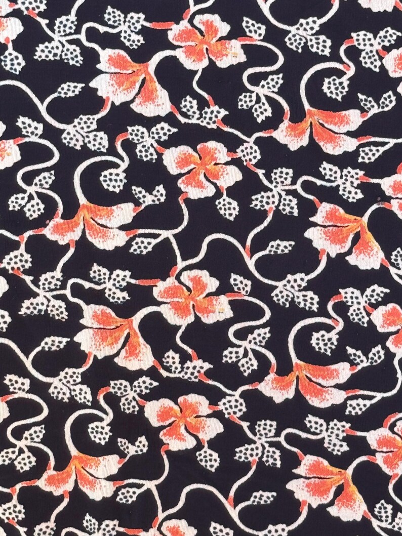 May include: A close-up of a fabric with a repeating floral pattern. The design features orange and white flowers with white vines and leaves against a dark navy blue background. The pattern is detailed and intricate.