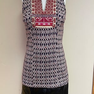 May include: A sleeveless dress with a black and white geometric pattern. The dress has a red and white embroidered neckline and a black faux leather skirt.