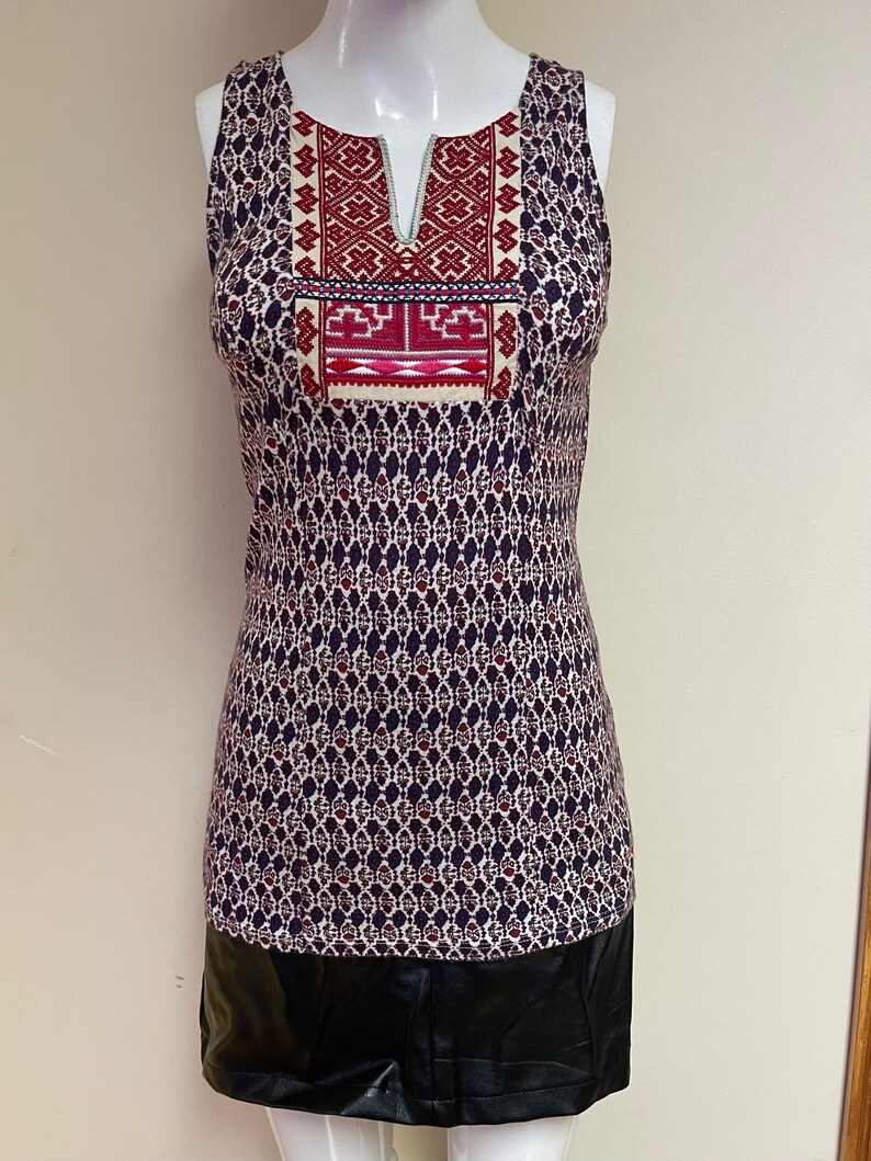 May include: A sleeveless dress with a black and white geometric pattern. The dress has a red and white embroidered neckline and a black faux leather skirt.