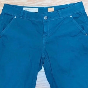 Puede incluir: Pantalones de color verde azulado oscuro con cierre de bot&oacute;n y bolsillos. Los pantalones tienen un dise&ntilde;o cl&aacute;sico con pernera recta y cintura de talle medio. La etiqueta dice "Hope and the Generation".