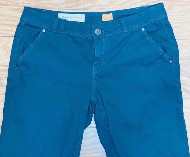 Puede incluir: Pantalones de color verde azulado oscuro con cierre de bot&oacute;n y bolsillos. Los pantalones tienen un dise&ntilde;o cl&aacute;sico con pernera recta y cintura de talle medio. La etiqueta dice "Hope and the Generation".