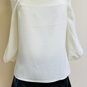 May include: A white blouse with puffed sleeves and a square neckline, paired with a black skirt.