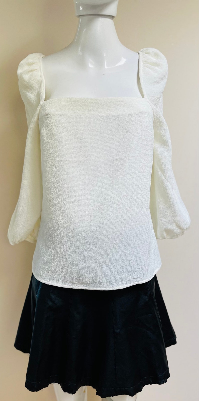 May include: A white blouse with puffed sleeves and a square neckline, paired with a black skirt.