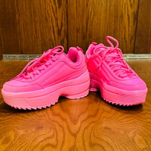 May include: A pair of bright pink platform sneakers with white laces. The sneakers have a chunky sole and a rounded toe.
