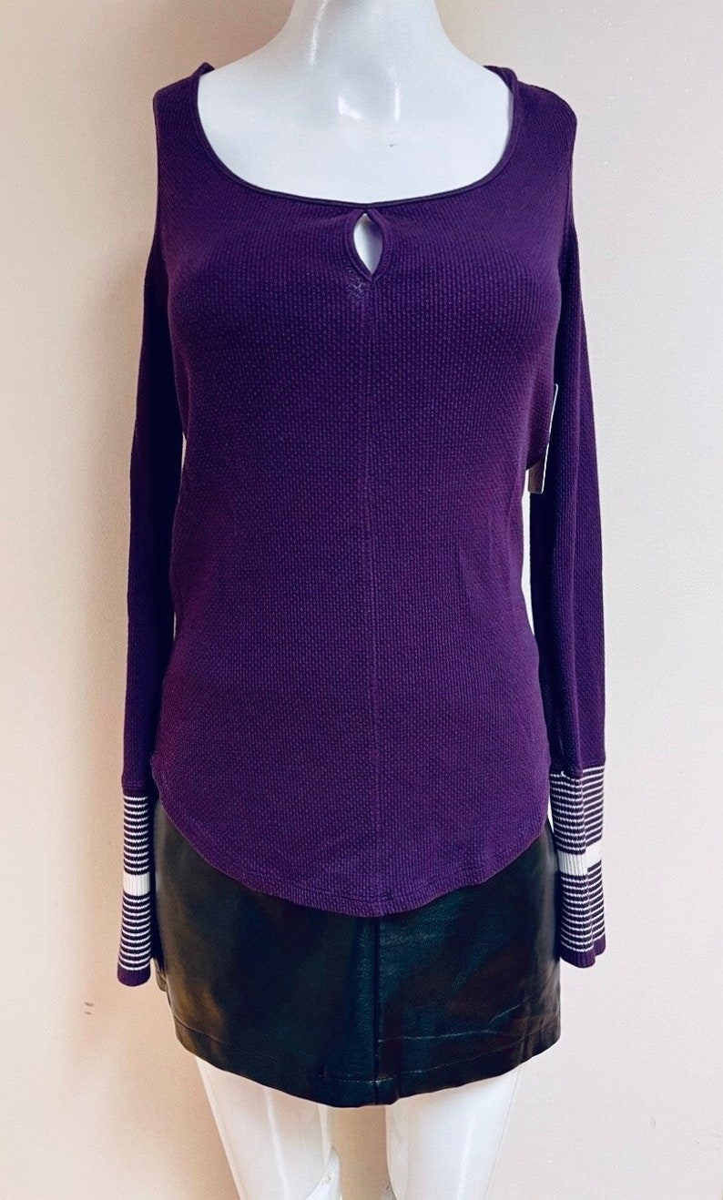 May include: A purple waffle knit long-sleeved shirt with a keyhole neckline and white striped cuffs. The shirt is on a white mannequin and has a relaxed fit.