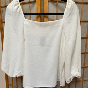 May include: A white, long-sleeved blouse with a square neckline and puffed sleeves.