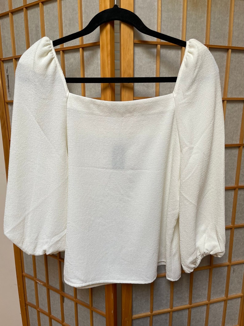 May include: A white, long-sleeved blouse with a square neckline and puffed sleeves.
