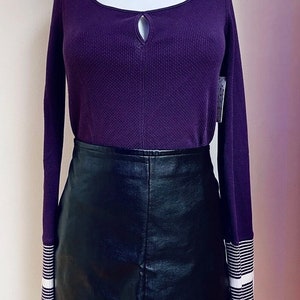 May include: A purple long-sleeved shirt with a keyhole neckline and white stripes on the cuffs, paired with a black leather mini skirt.