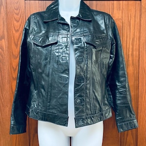 May include: A black leather jacket with a button-up front and a classic denim jacket style. The jacket has two flap pockets on the chest and two pockets at the waist.