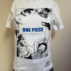 May include: White t-shirt featuring a black and white graphic print of characters from the anime One Piece. The graphic includes the text "One Piece" and a wanted poster with the text "Wanted One Piece".