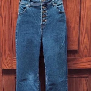 May include: Blue denim jeans with a button-up fly and a wide leg. The jeans are displayed on a mannequin. The jeans have two front pockets and two back pockets. The jeans are a medium wash.