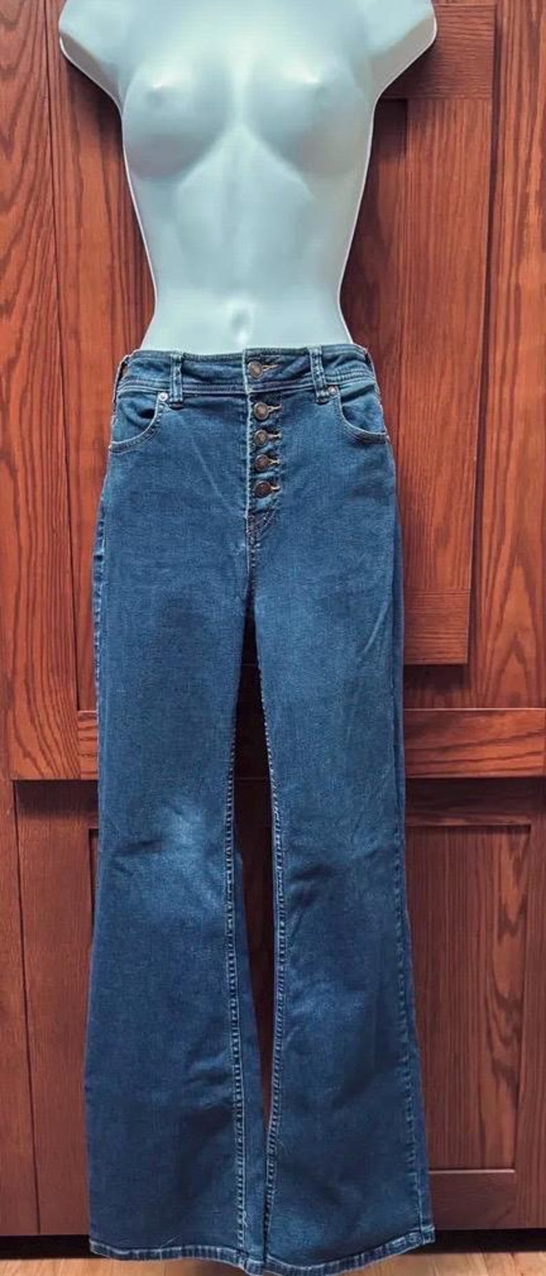 May include: Blue denim jeans with a button-up fly and a wide leg. The jeans are displayed on a mannequin. The jeans have two front pockets and two back pockets. The jeans are a medium wash.