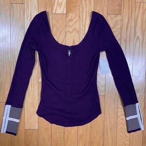 May include: A long-sleeved, purple, ribbed top with a scoop neck and white striped cuffs.