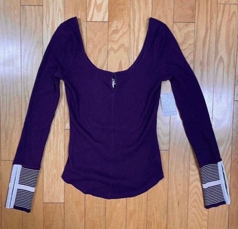 May include: A long-sleeved, purple, ribbed top with a scoop neck and white striped cuffs.