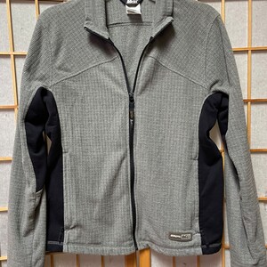 May include: A gray and black zippered fleece jacket with a  "REI" logo on the lower right side.