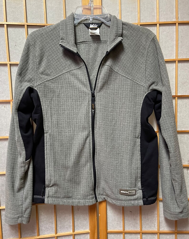 May include: A gray and black zippered fleece jacket with a  "REI" logo on the lower right side.