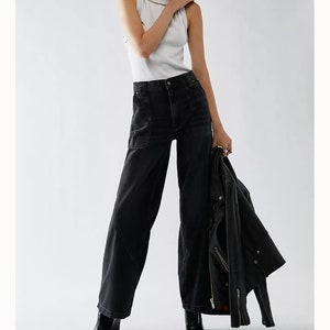 May include: Black high-rise jeans with a relaxed fit and multiple pockets. The jeans are shown on a model wearing a white tank top and a black leather jacket. The text "Shop all We The Free" is visible in the image.