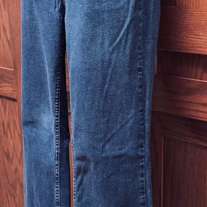 May include: Blue denim jeans with a button-up fly. The jeans have a classic five-pocket design and a straight leg. The buttons are a bronze color. The jeans are made of a medium-weight denim material.