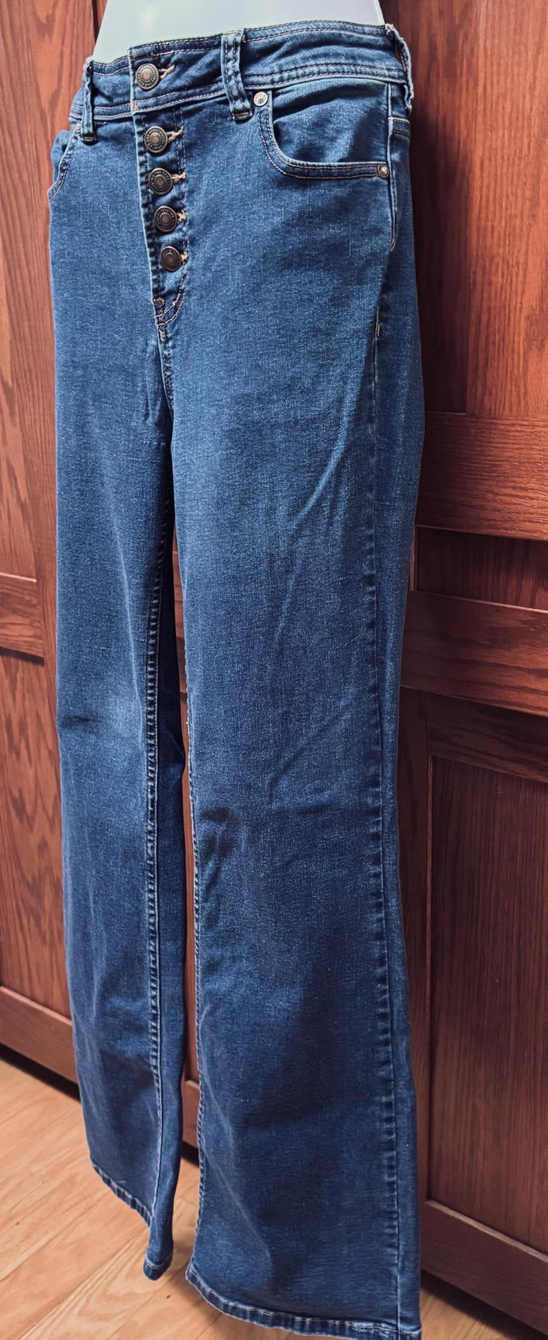 May include: Blue denim jeans with a button-up fly. The jeans have a classic five-pocket design and a straight leg. The buttons are a bronze color. The jeans are made of a medium-weight denim material.