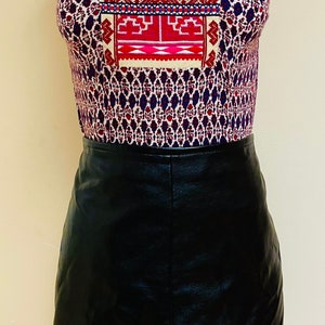 May include: A sleeveless top with a geometric pattern in shades of red, blue, and white. The top has a V-neck and a black leather skirt.