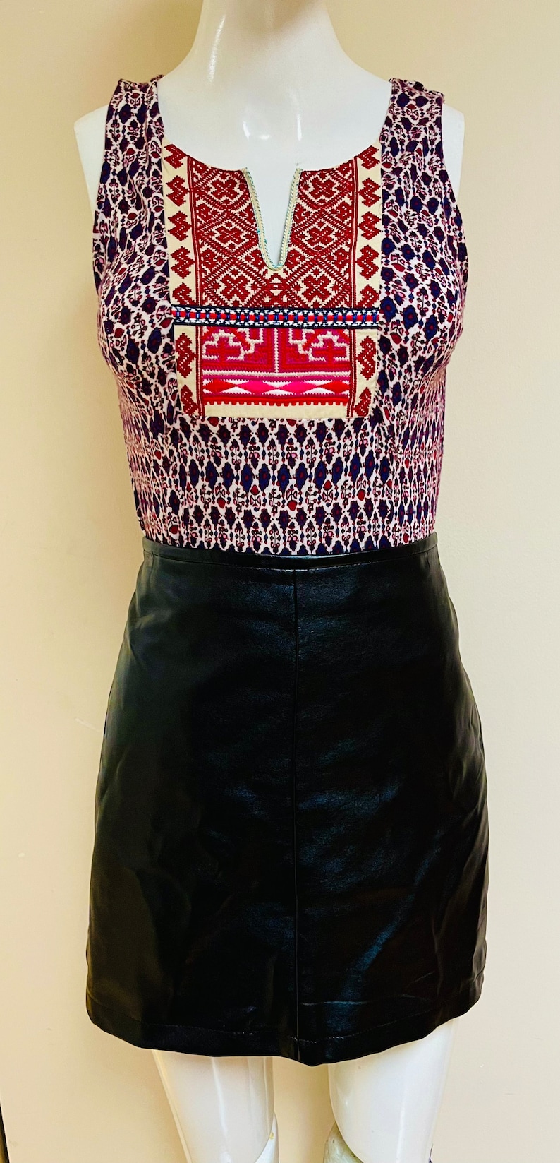 May include: A sleeveless top with a geometric pattern in shades of red, blue, and white. The top has a V-neck and a black leather skirt.