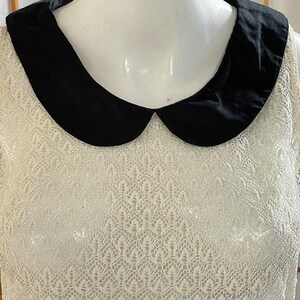 May include: A white lace sleeveless top with a black Peter Pan collar.