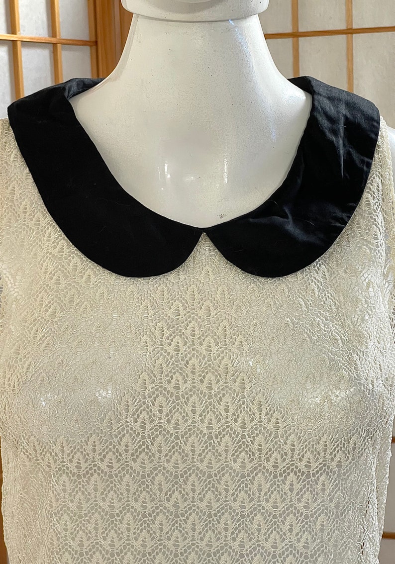 May include: A white lace sleeveless top with a black Peter Pan collar.