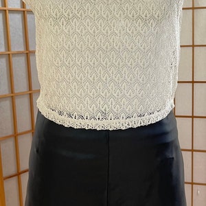 May include: A white crochet top with a black Peter Pan collar and a black faux leather skirt.