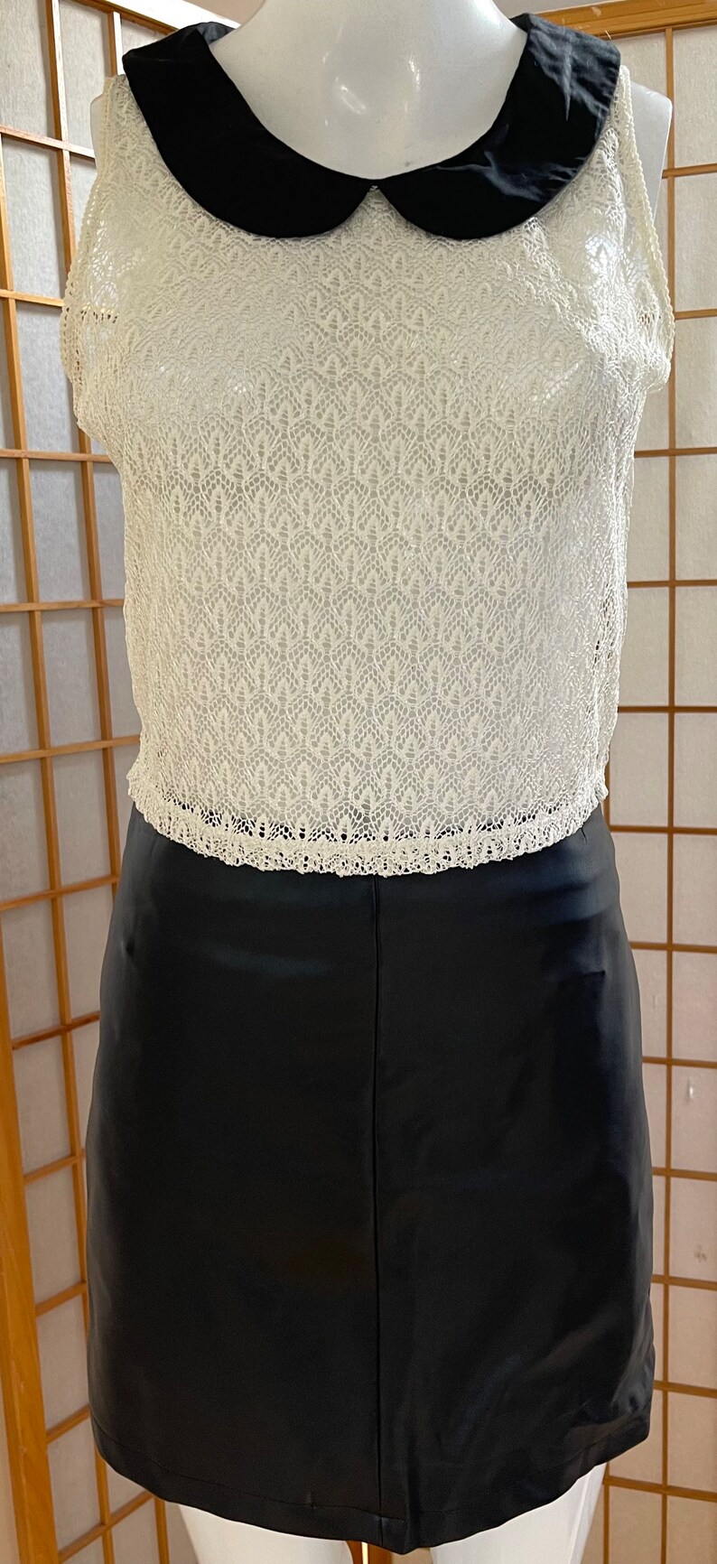 May include: A white crochet top with a black Peter Pan collar and a black faux leather skirt.